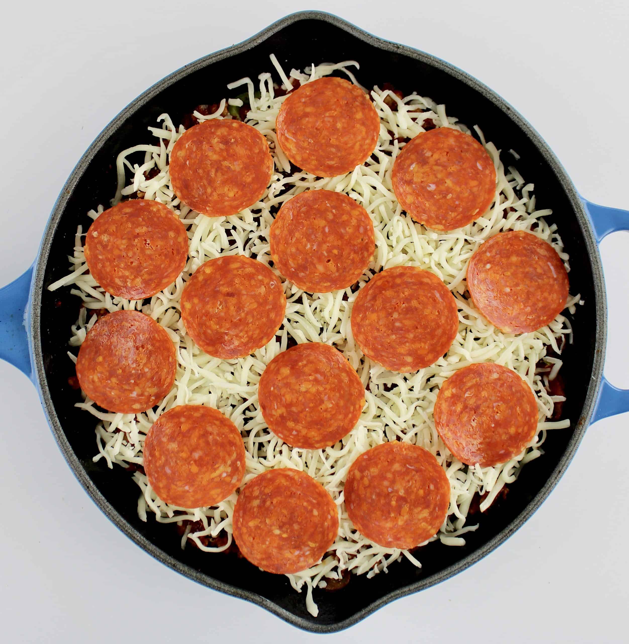unbaked crustless pizza in skillet with shredded cheese and pepperoni