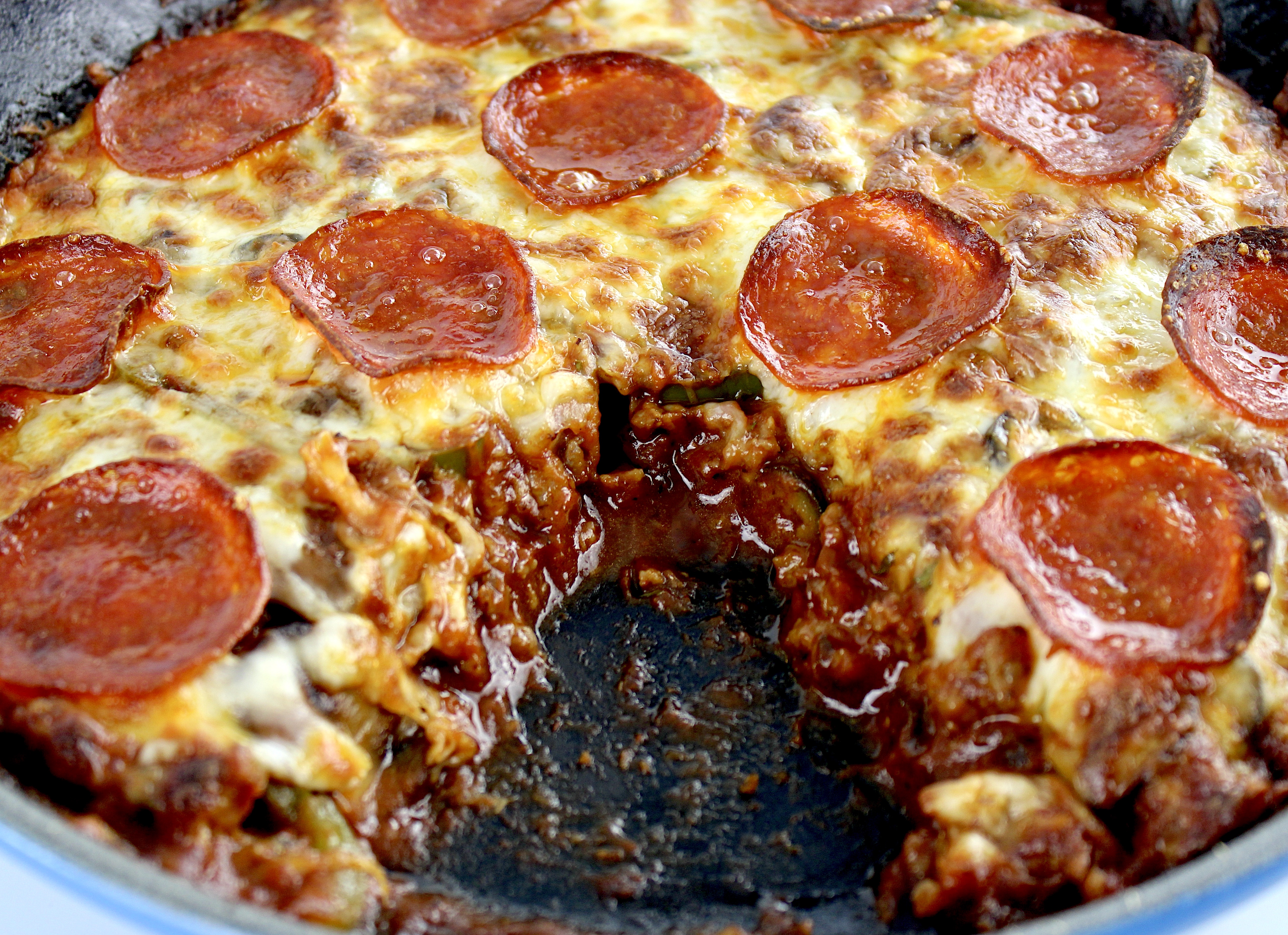 closeup of crustless pepperoni pizza in skillet with piece missing