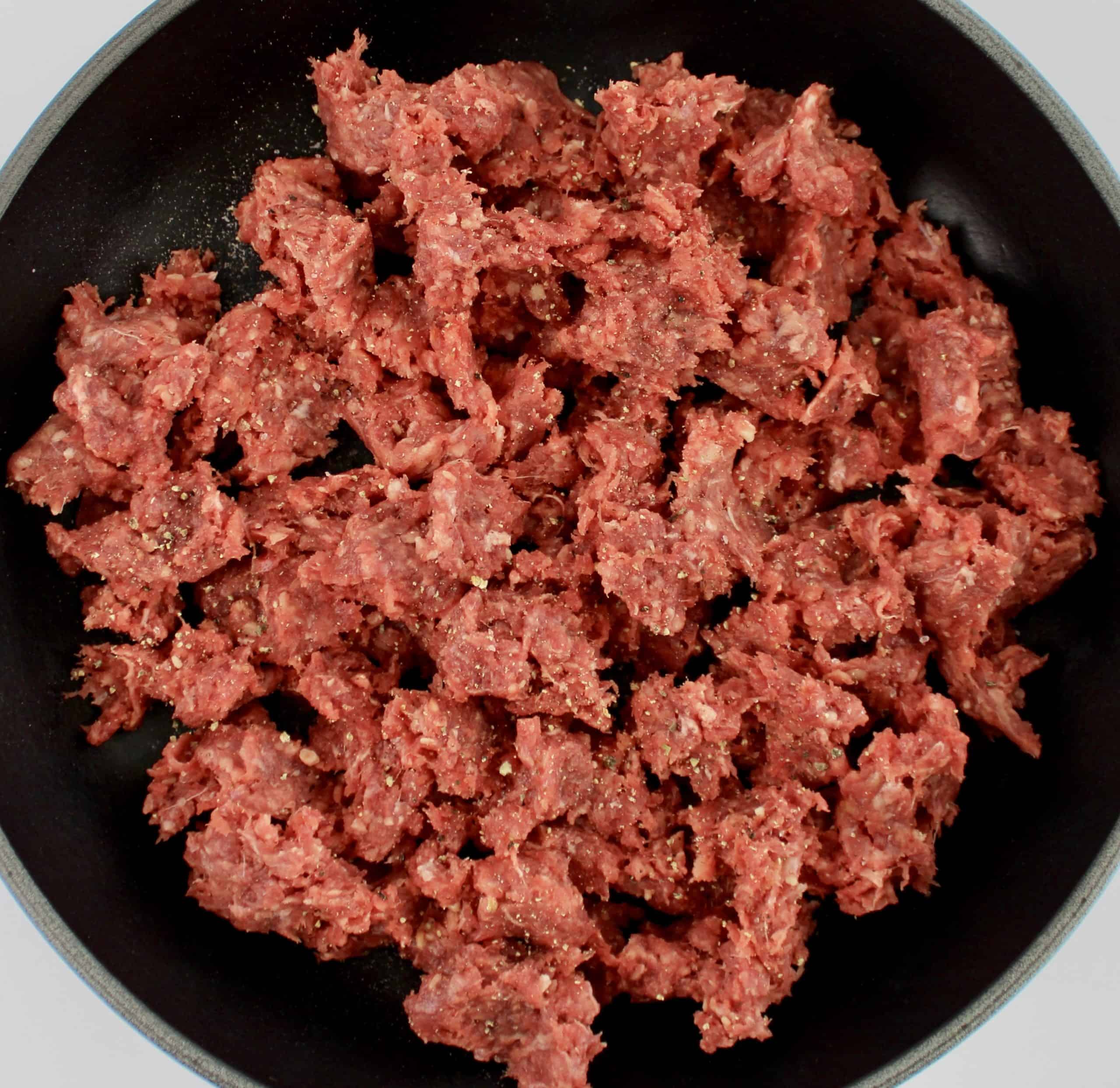 raw ground beef with salt and pepper in skillet