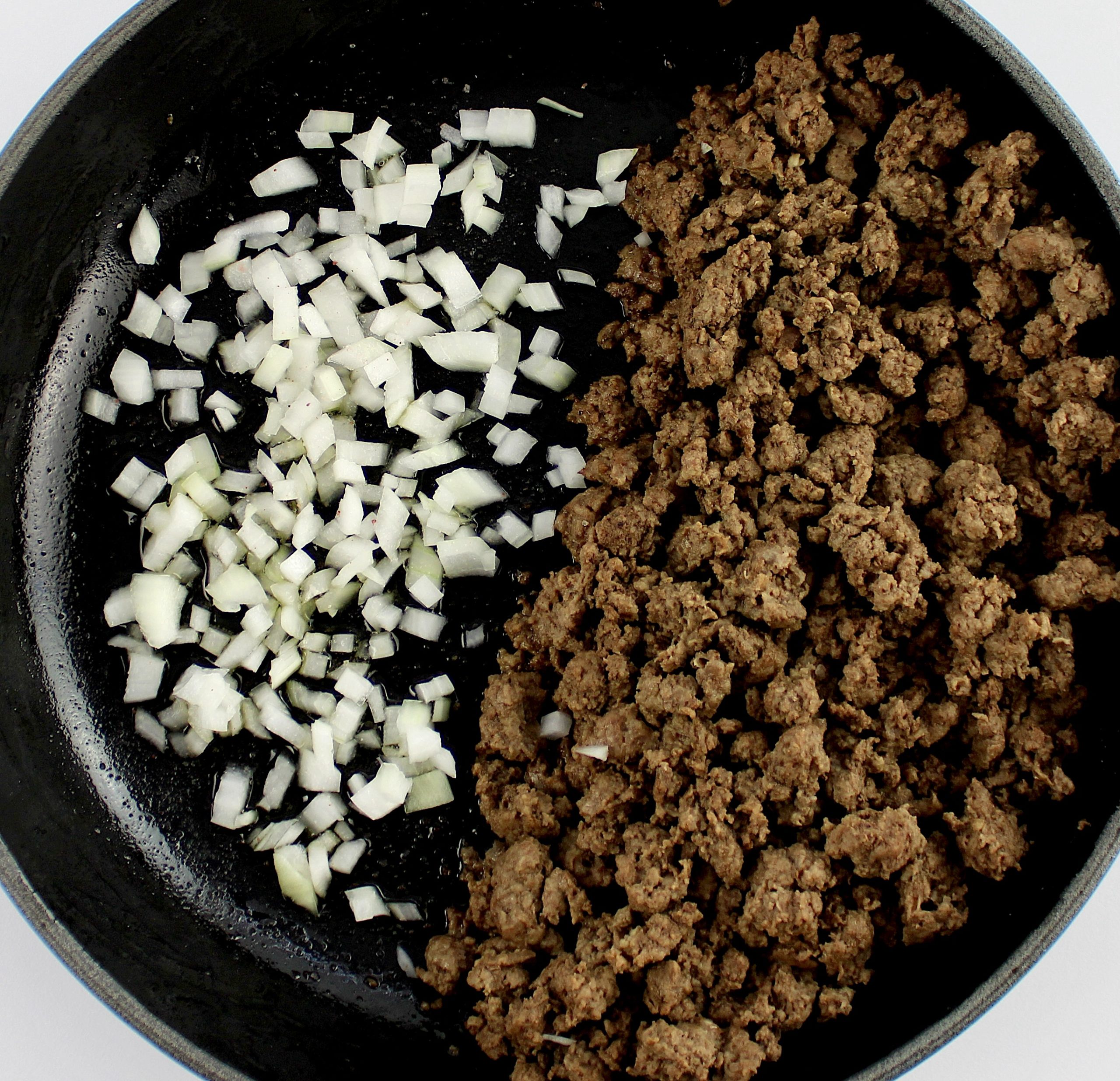 cooked ground beef on right side with raw minced onion on left side of skillet