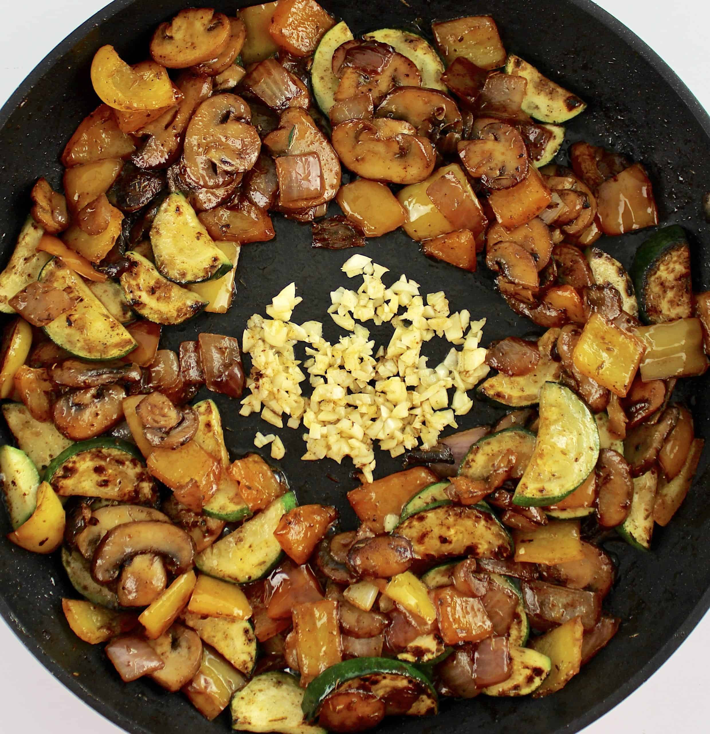 Sautéed veggies in skillet with minced garlic in the center