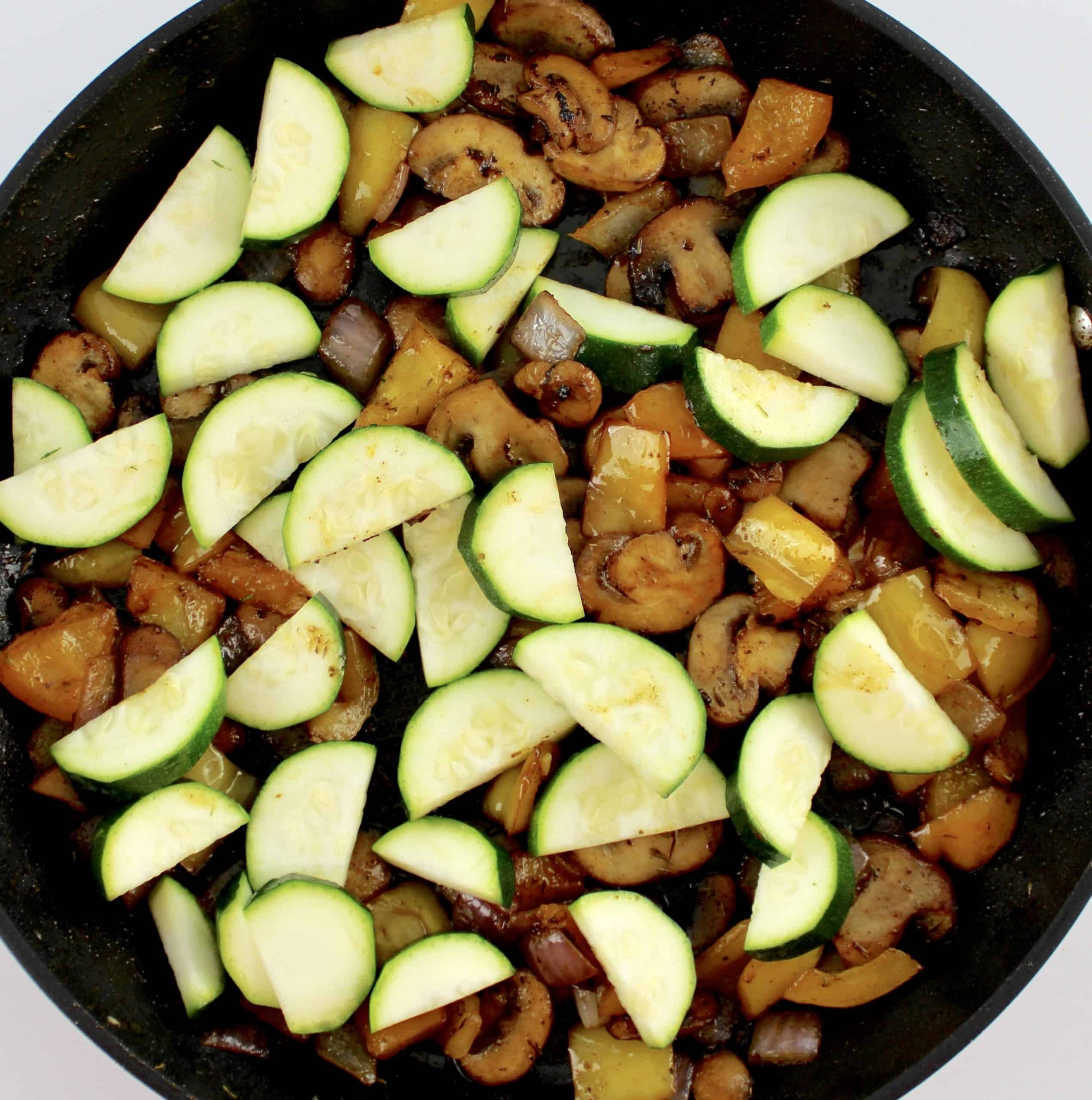sauteed veggies in skillet with sliced raw Zucchini 