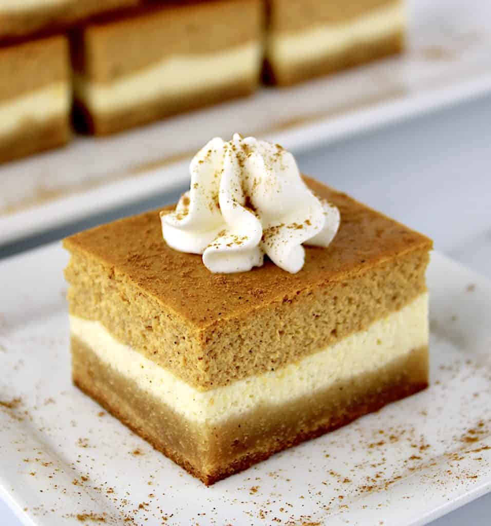 Keto Pumpkin Cheesecake Bar on white plate with whip cream on top and dash of cinnamon sprinkled around
