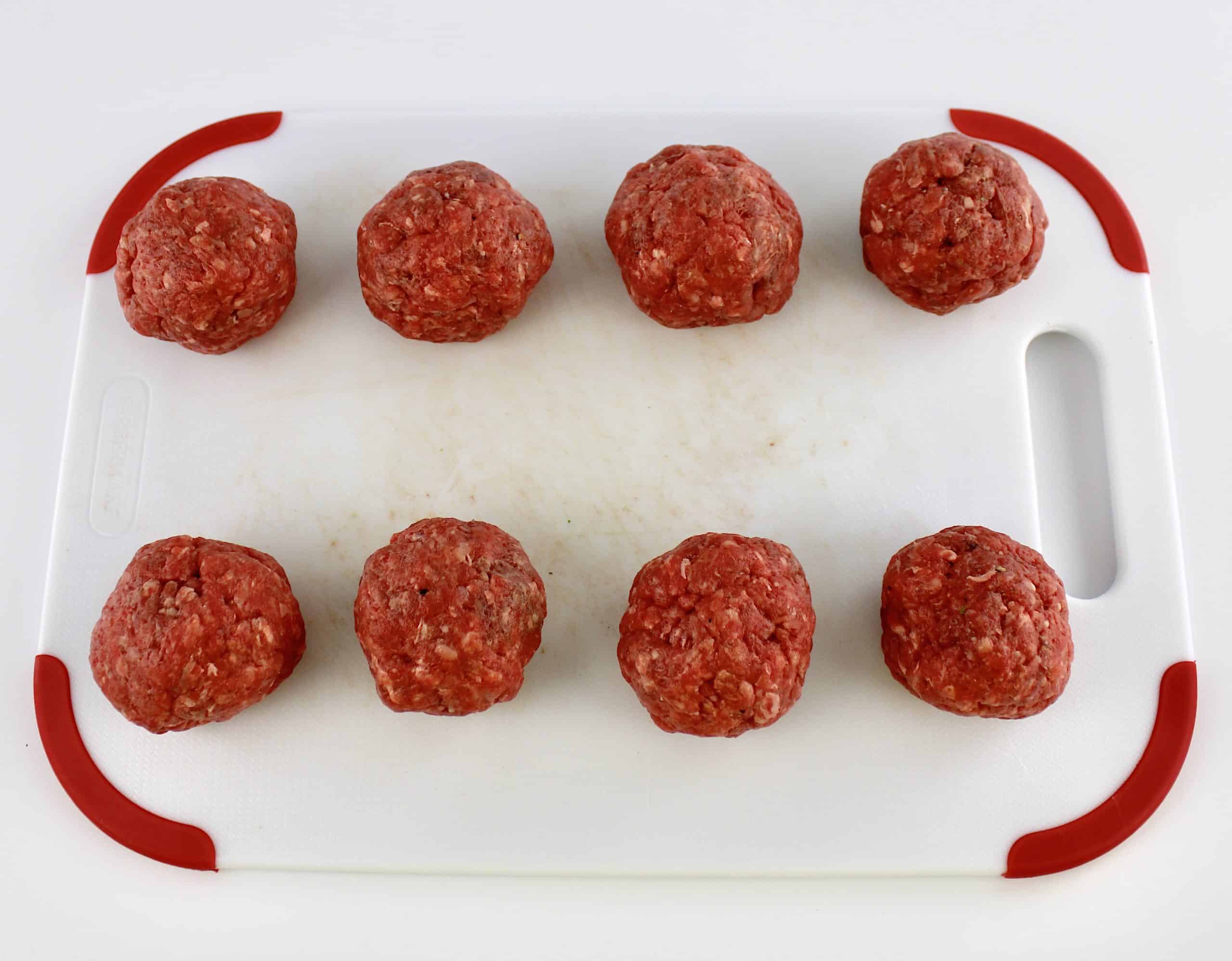 8 balls of ground beef on white cutting board with red trim