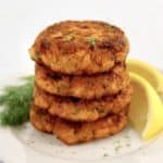 stack of Salmon Patties on white plate with lemon and fresh dill on side
