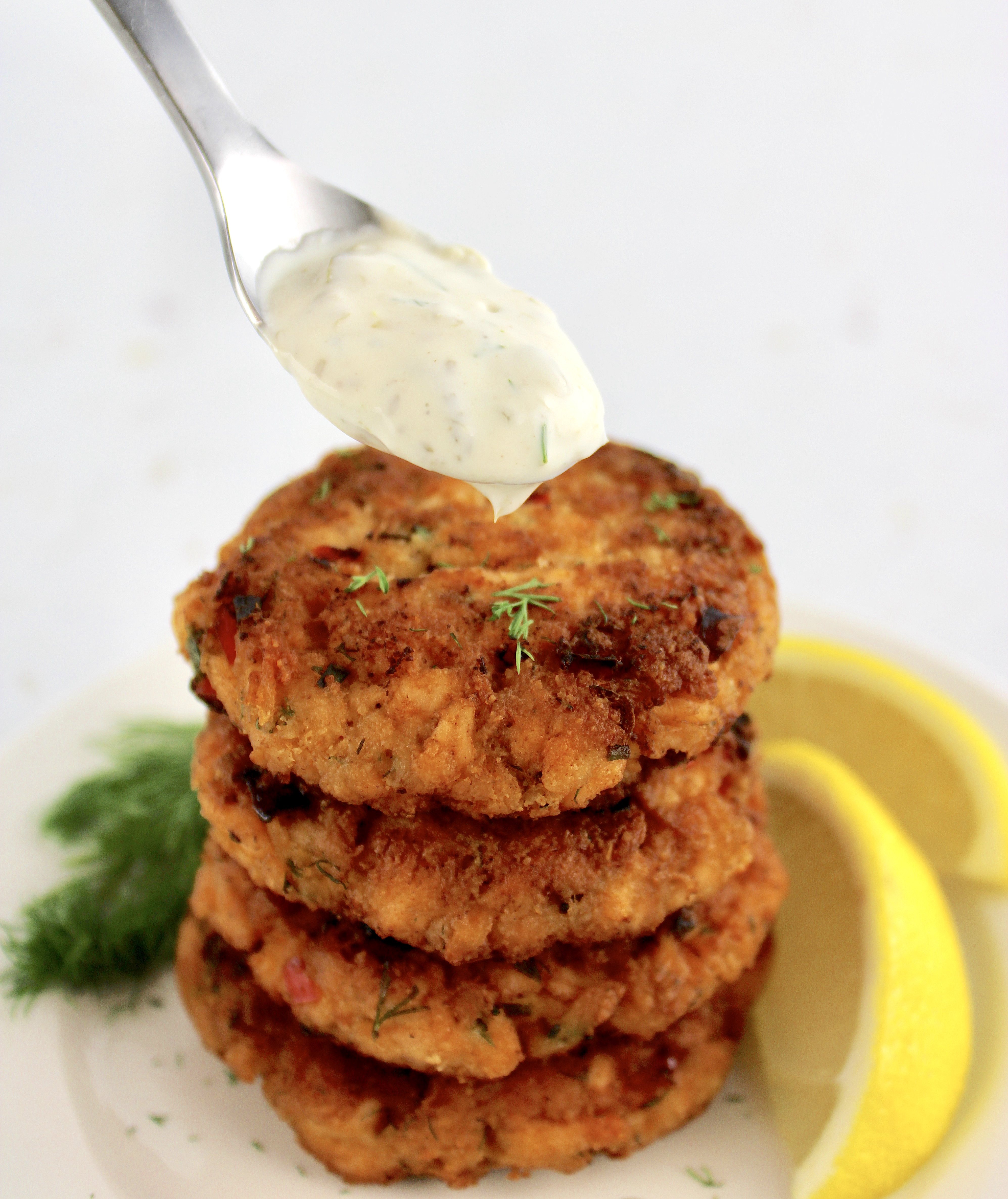 stack of 4 salmon patties with dill sauce being spooned over the top