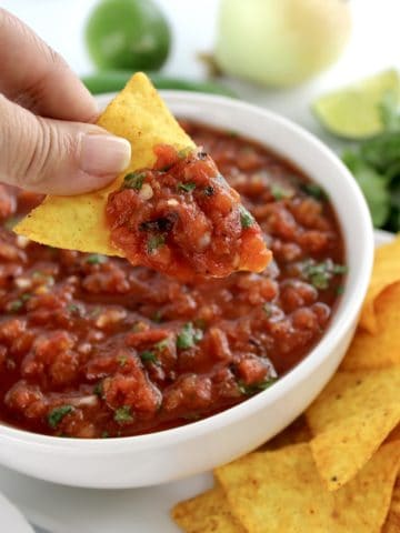 tortilla chip scooping up salsa in white bowl with chips in background