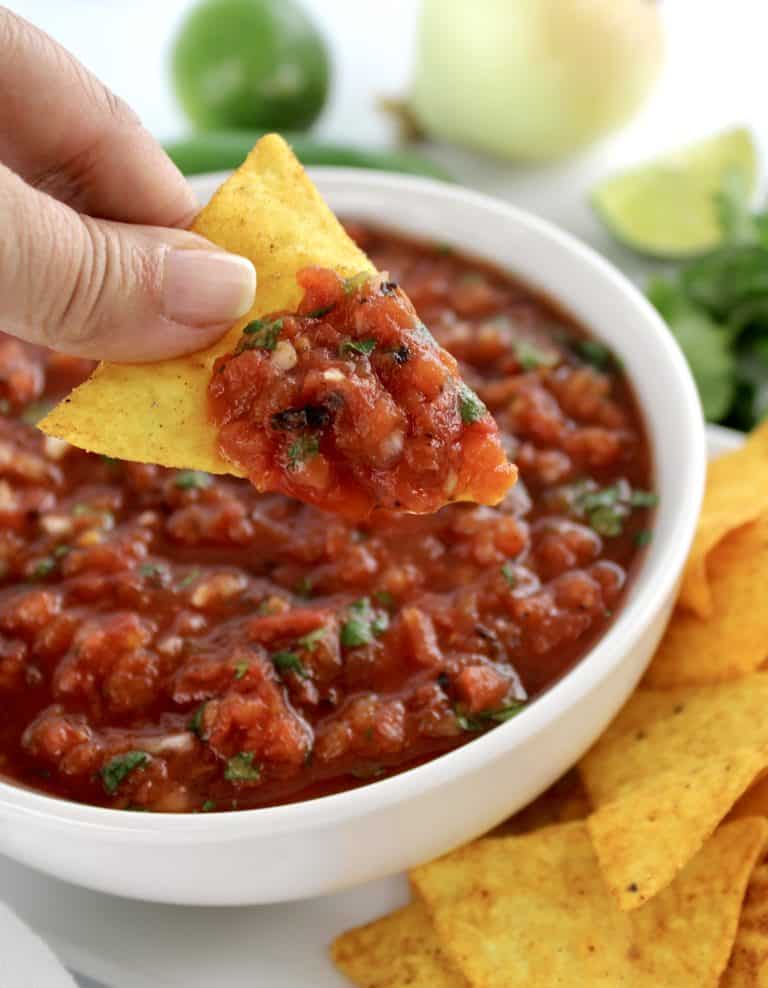 tortilla chip scooping up salsa in white bowl with chips in background