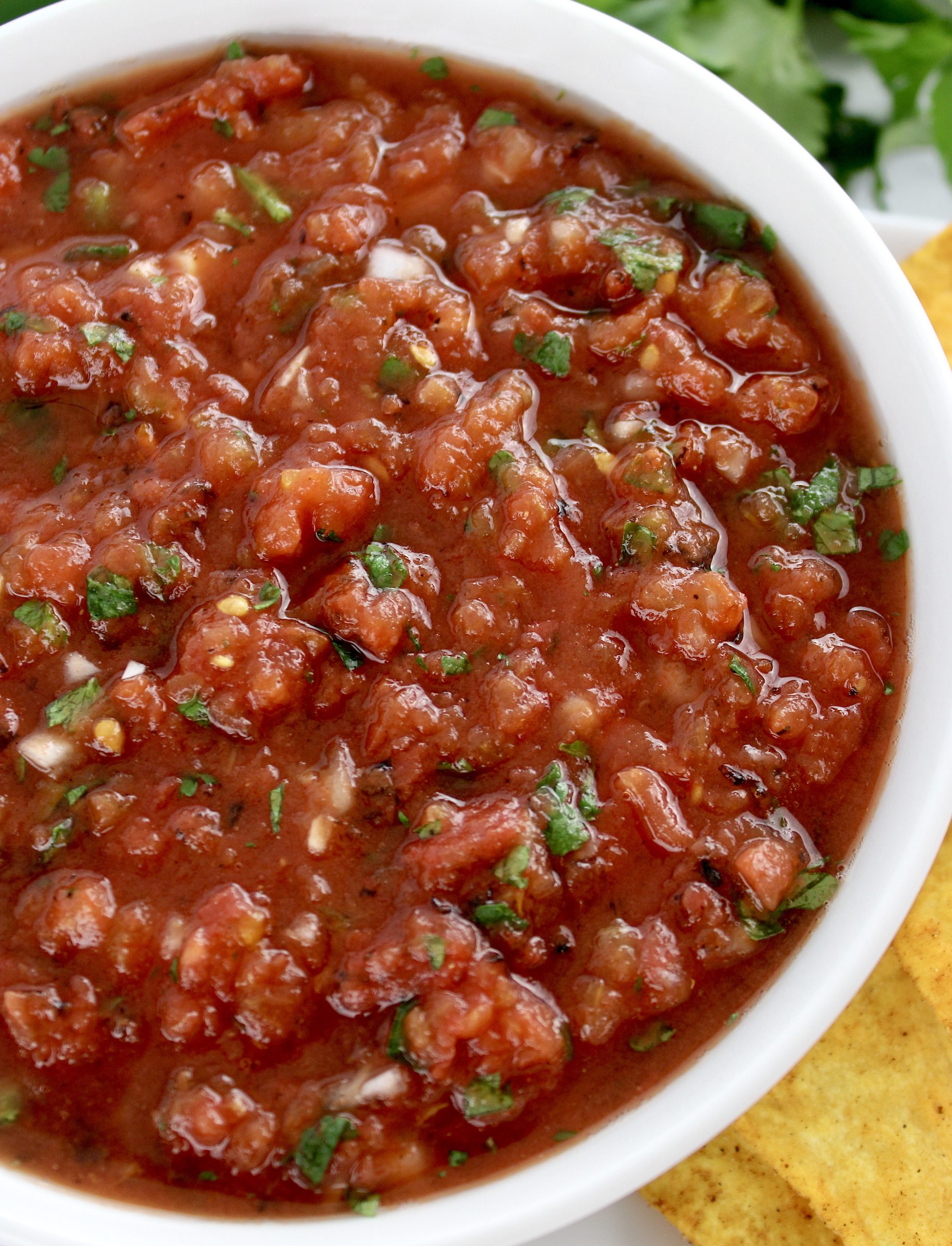 overhead view of salsa in white bowl with chips and cilantro in background