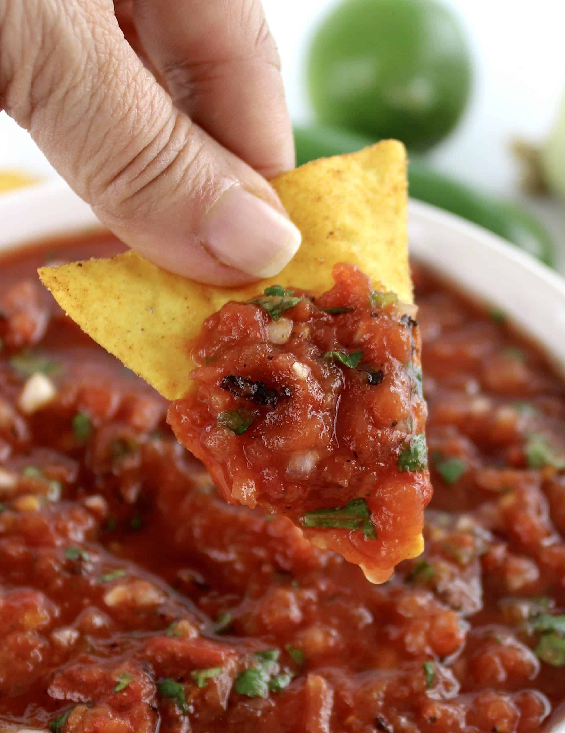 tortilla chip scooping up salsa in white bowl with chips in background
