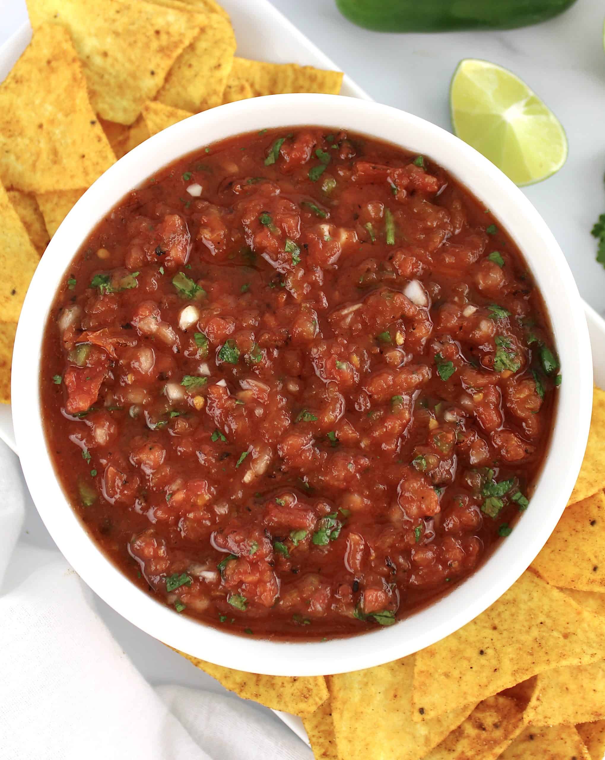 overhead view of salsa in white bowl with tortilla chips on sides