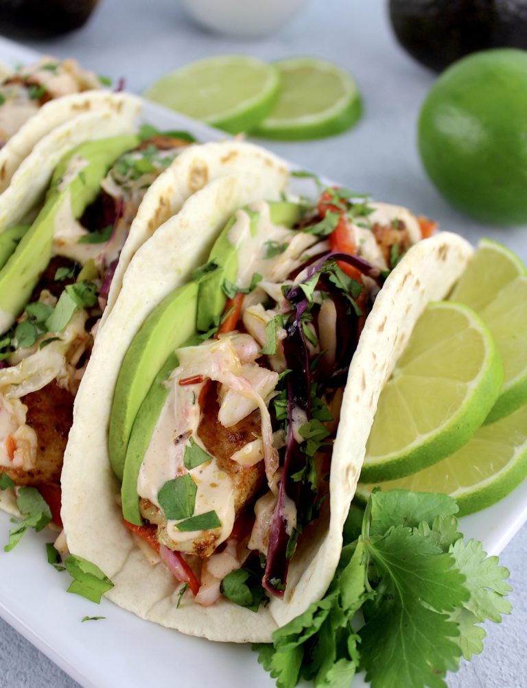 Mahi Mahi Tacos in white plate with avocado slices and lime on side