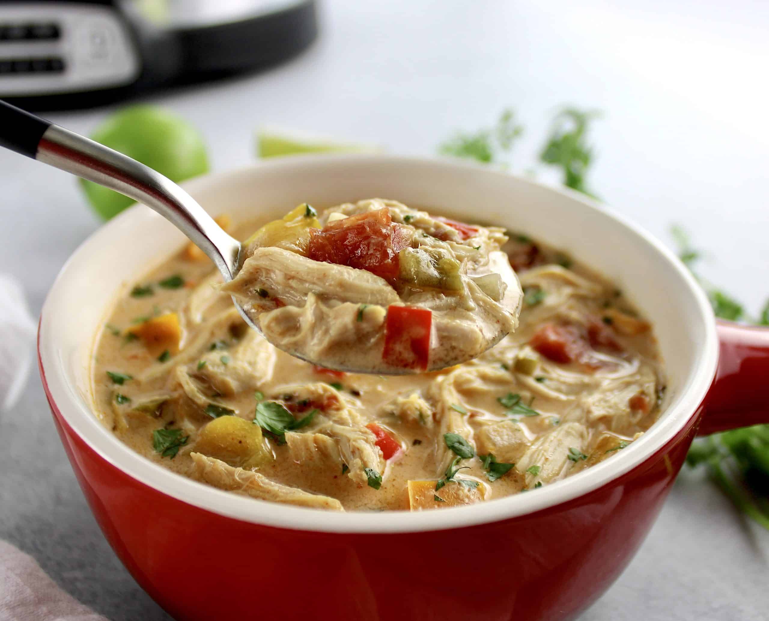 Slow Cooker Chicken Fajita Soup in red crock with spoon holding up some