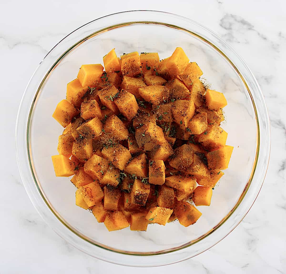 butternut squash cubes in glass bowl with spices and herbs on top