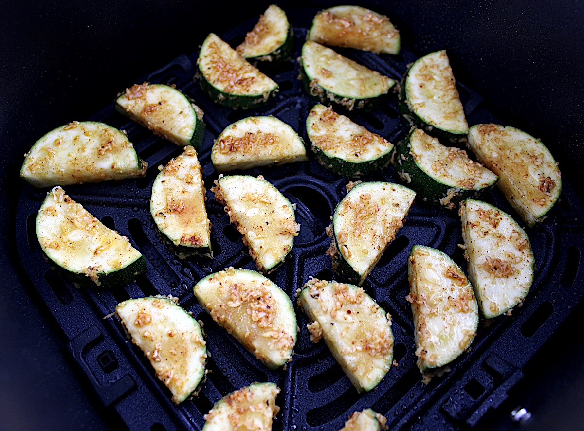 slices of zucchini with spices and parmesan in air fryer basket uncooked