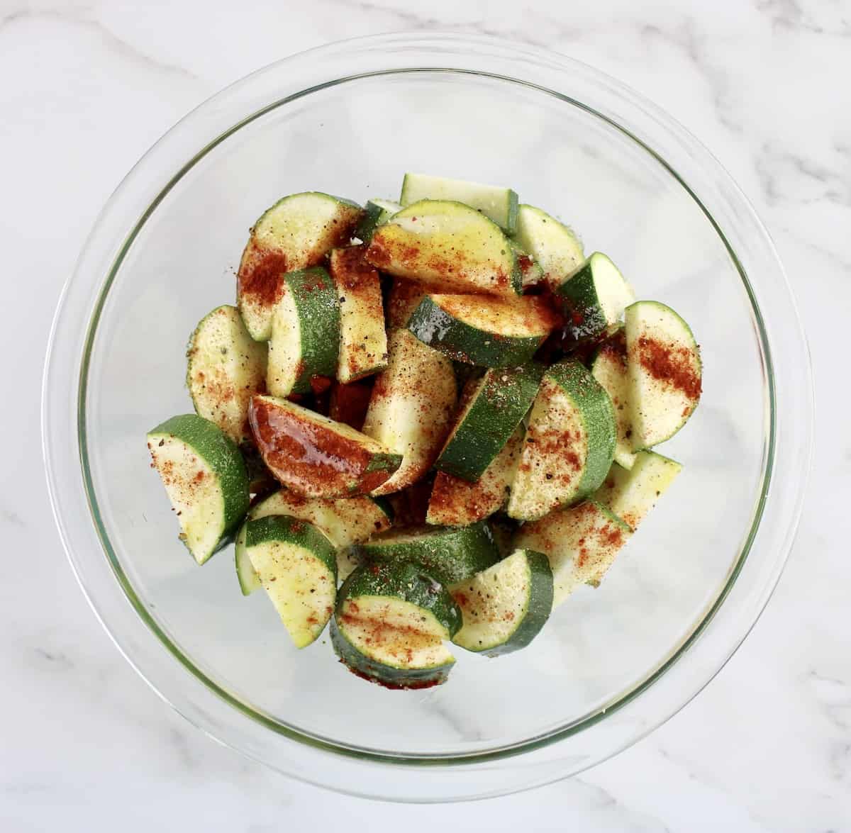 sliced zucchini in glass bowl with spices and olive oil on top