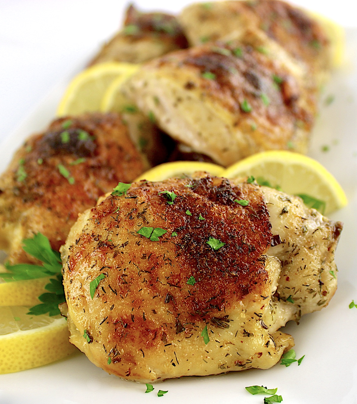 closeup of Baked Chicken Thigh with chopped parsley and lemon slices on side