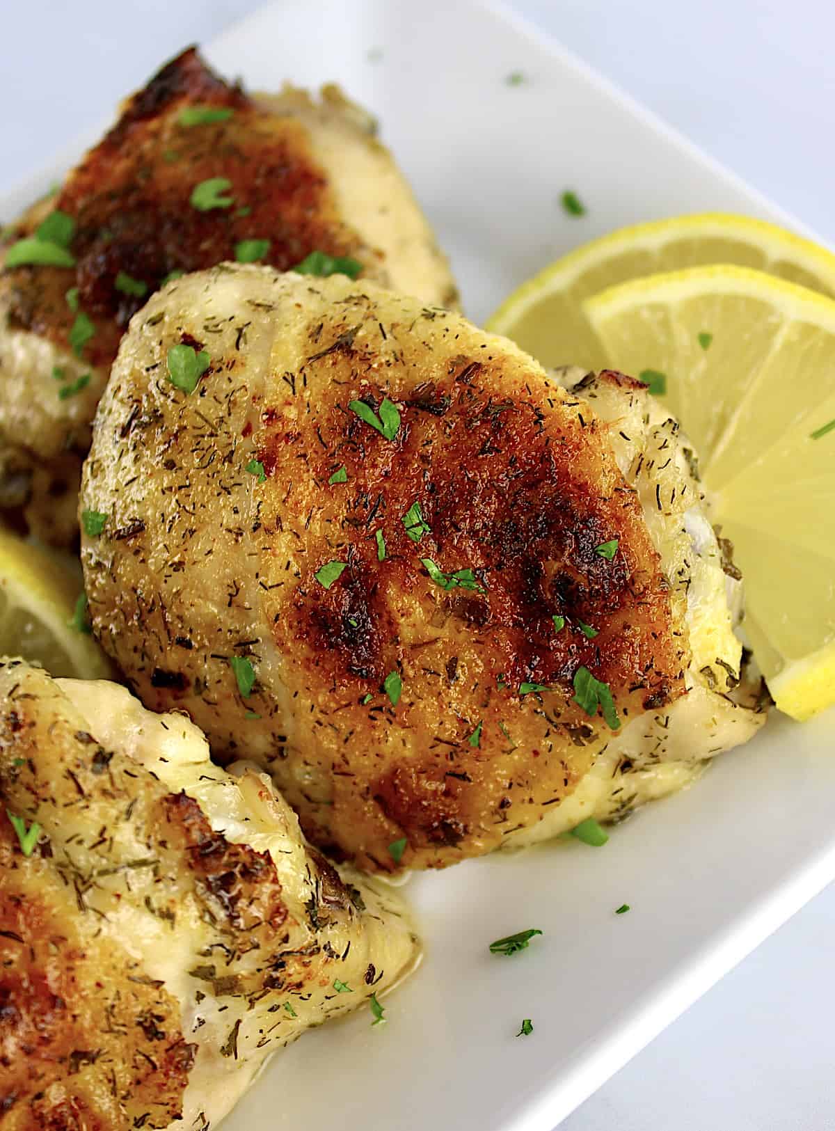 closeup of Baked Chicken Thigh with chopped parsley and lemon slices on side