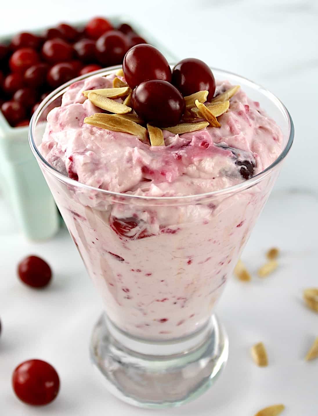 Cranberry Cheesecake Fluff in glass with cranberries in background and toasted almonds on top