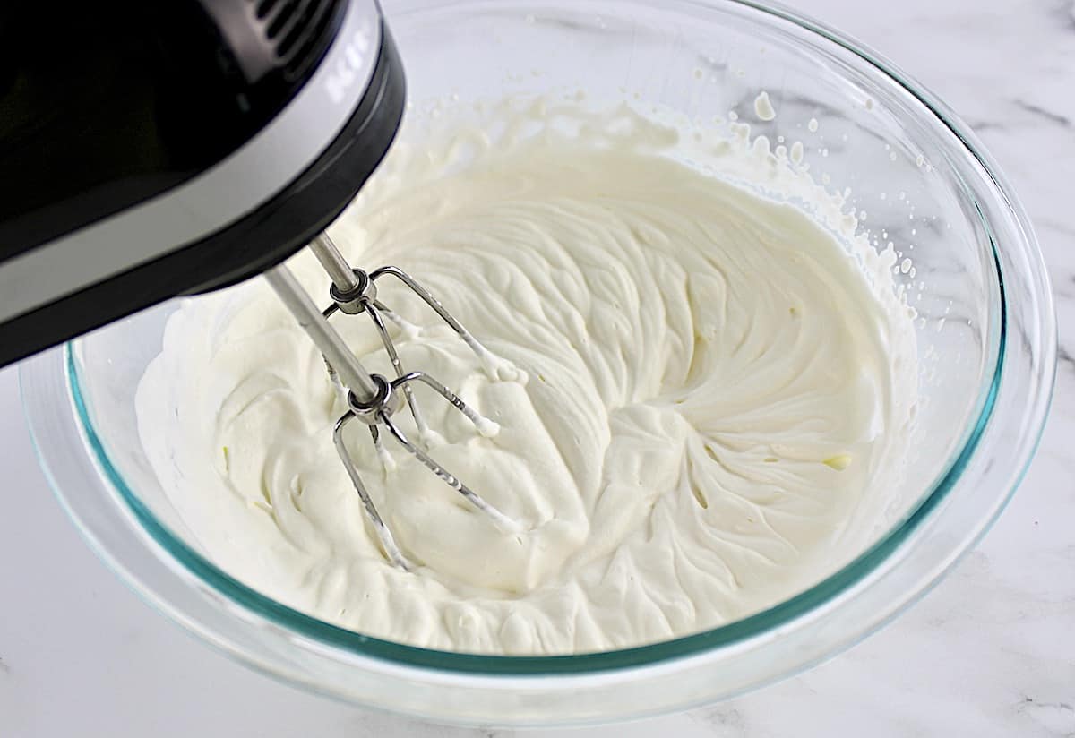 cream being whipped by hand mixer in glass bowl