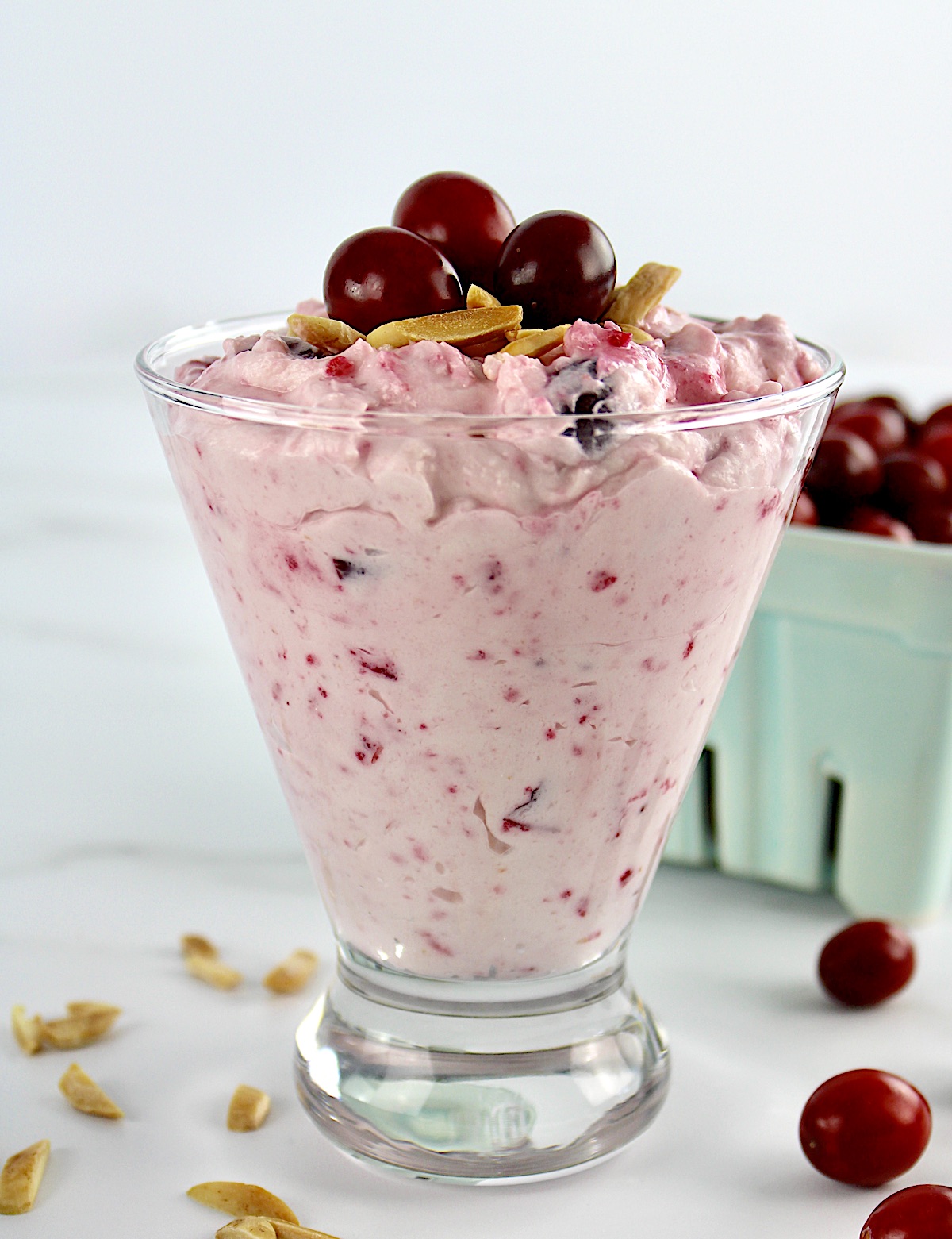 Cranberry Cheesecake Fluff in glass with cranberries in background and toasted almonds on top