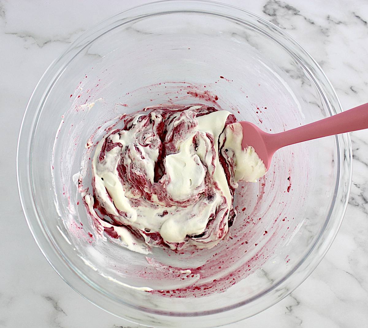 Cranberry Cheesecake Fluff being folder into whip cream in glass bowl with pink spatula