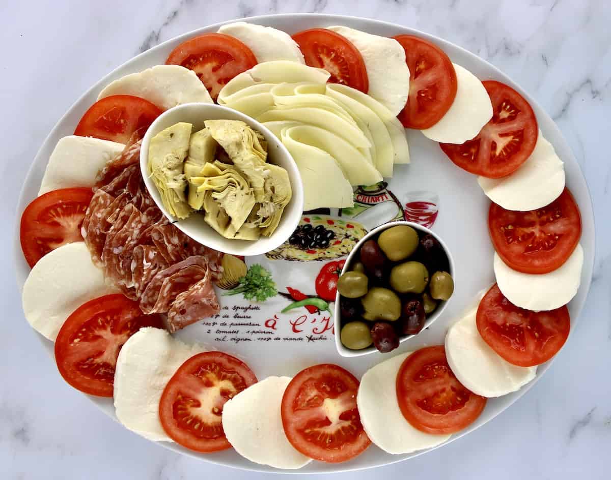 slices of mozzarella cheese and tomatoes around the edge of a platter with olives cheese and artichoke hearts in the center