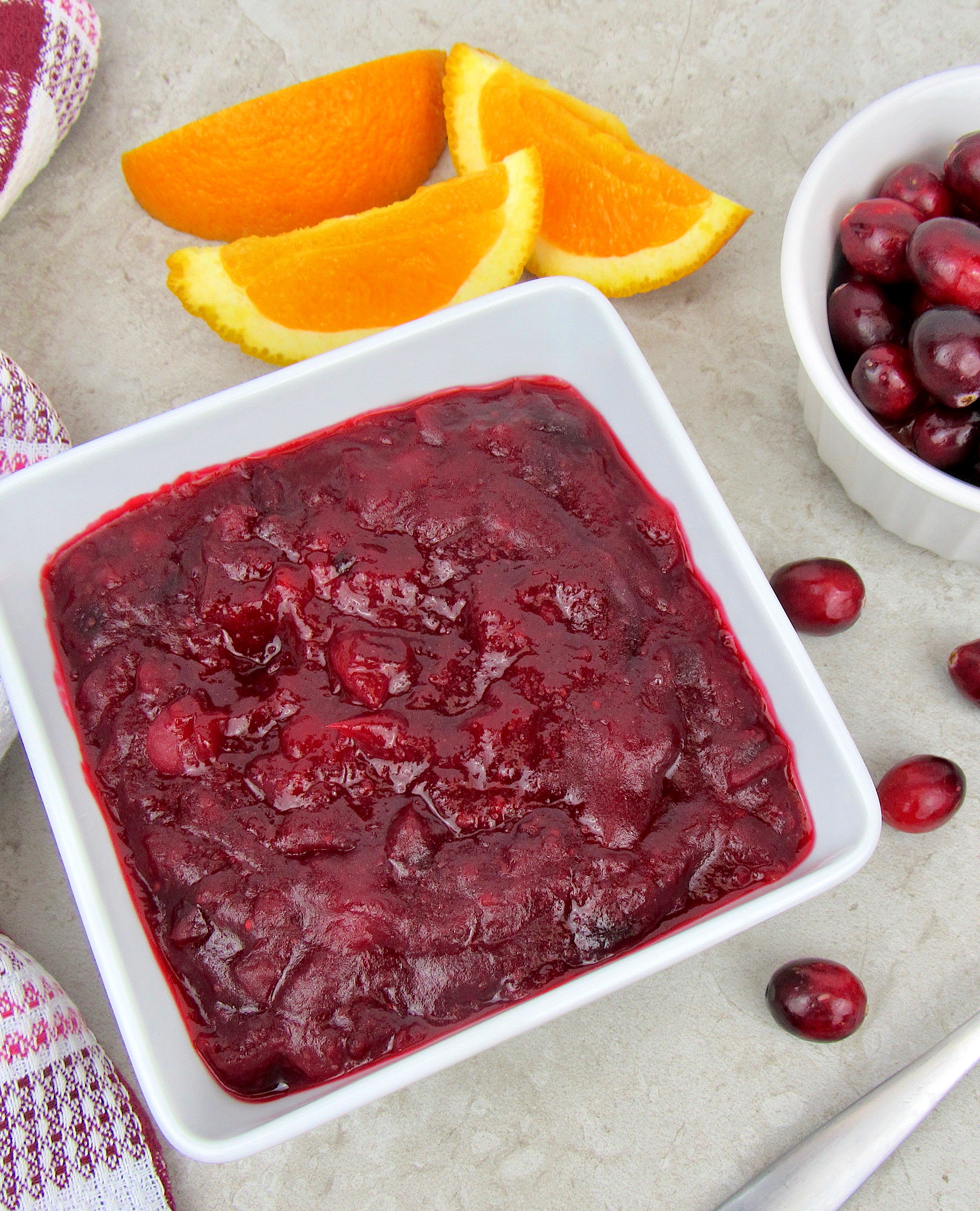 Keto Cranberry Sauce in white square bowl with sliced oranges and cranberries in background