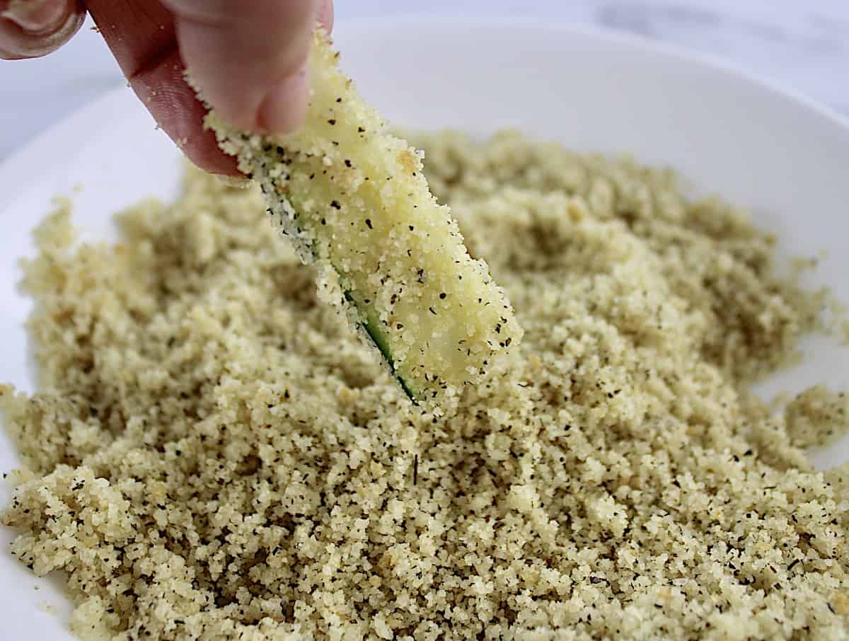 zucchini stick being dipped into breading