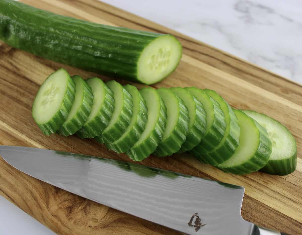 sliced English cucumber on cutting board with knife