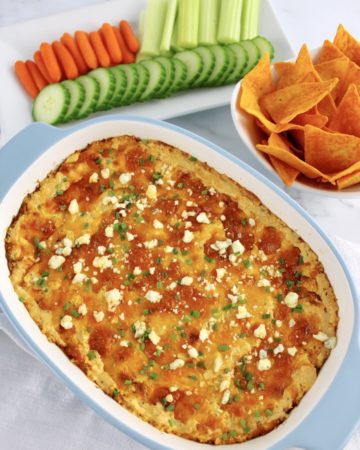 Buffalo Chicken Dip in baking dish with sliced veggies and tortilla chips in background