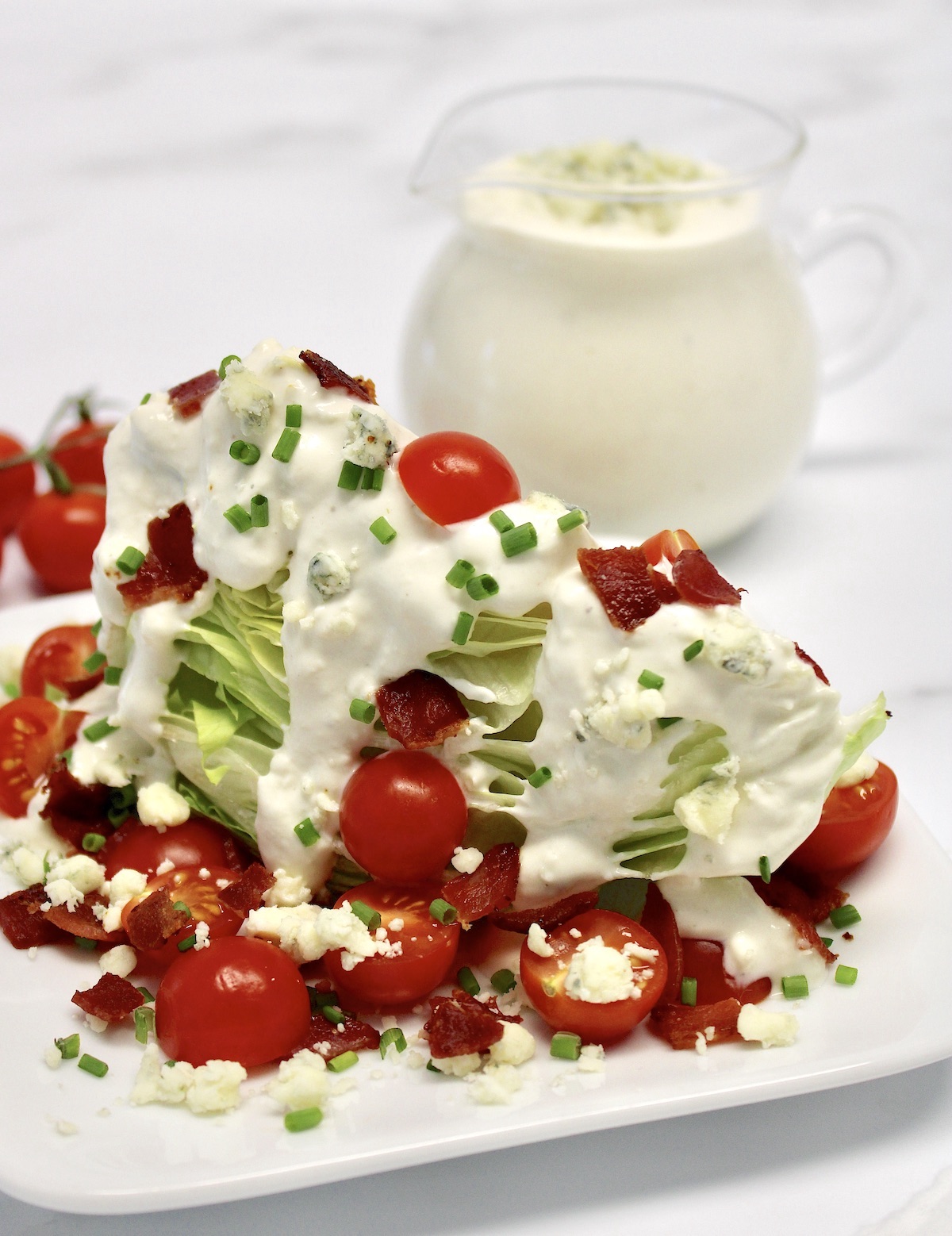 Classic Wedge Salad on white plate with blue cheese dressing in background