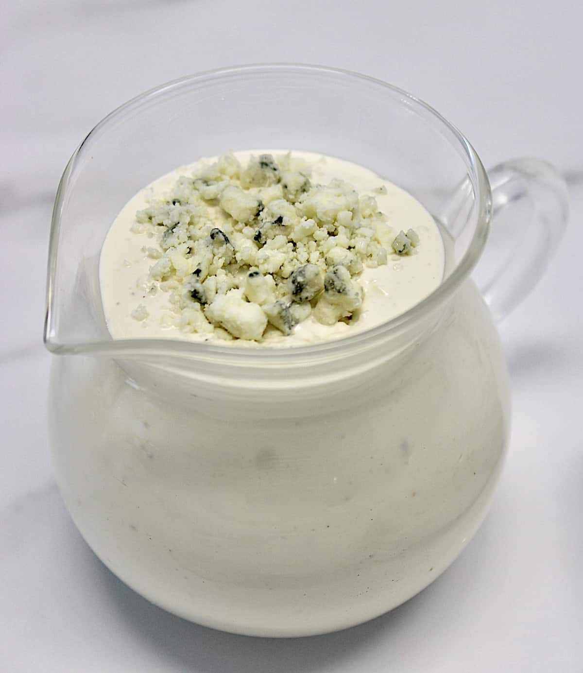 blue cheese dressing in glass pitcher with blue cheese crumbles on top