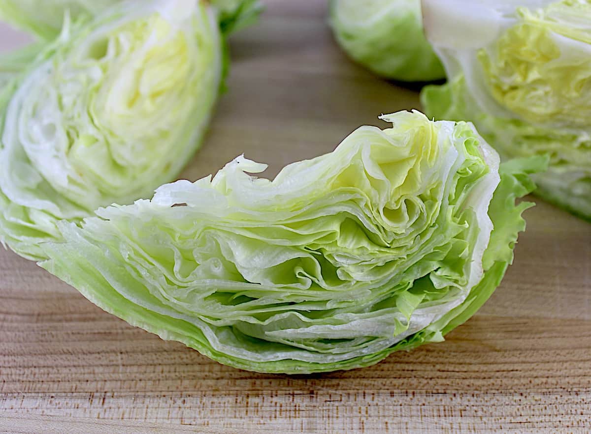 closeup of a wedge of iceberg lettuce on cutting board with more lettuce in background