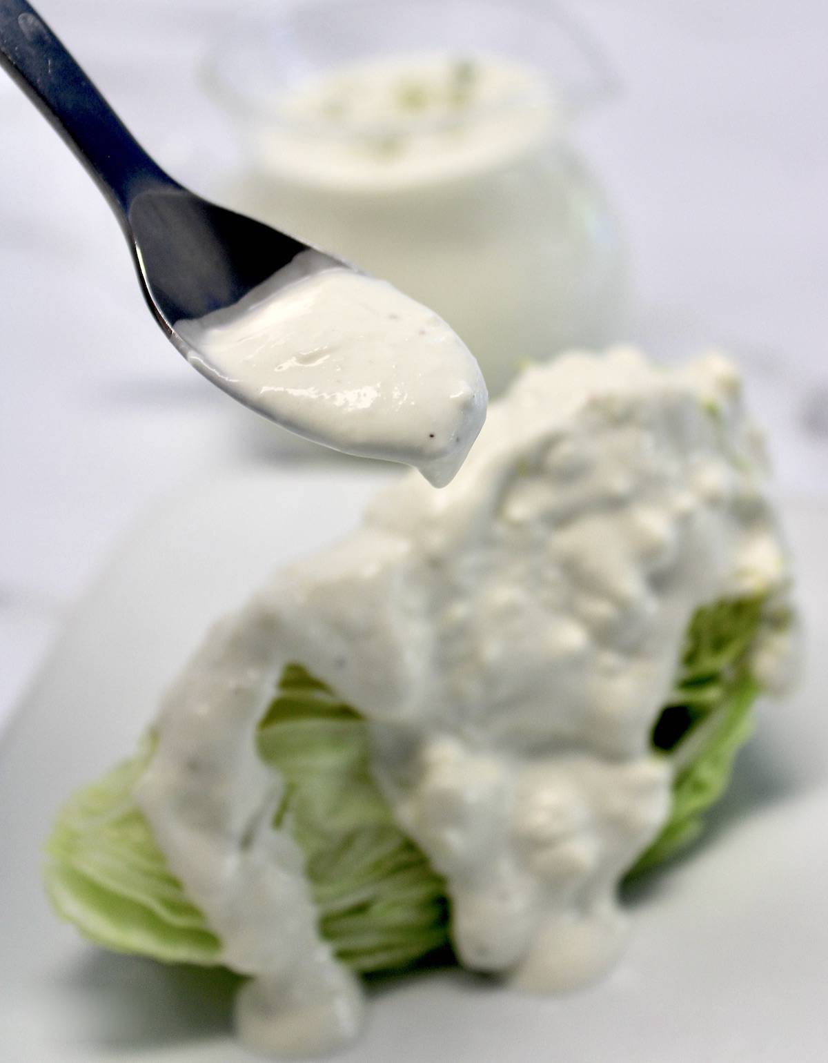 Keto Blue Cheese Dressing being spooned over iceberg wedge on white plate