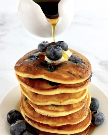 stack of Keto Blueberry Pancakes with blueberries on top and sides with syrup being poured over top