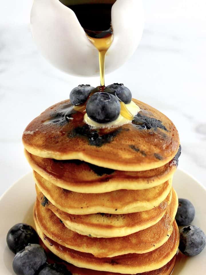 stack of Keto Blueberry Pancakes with blueberries on top and sides with syrup being poured over top