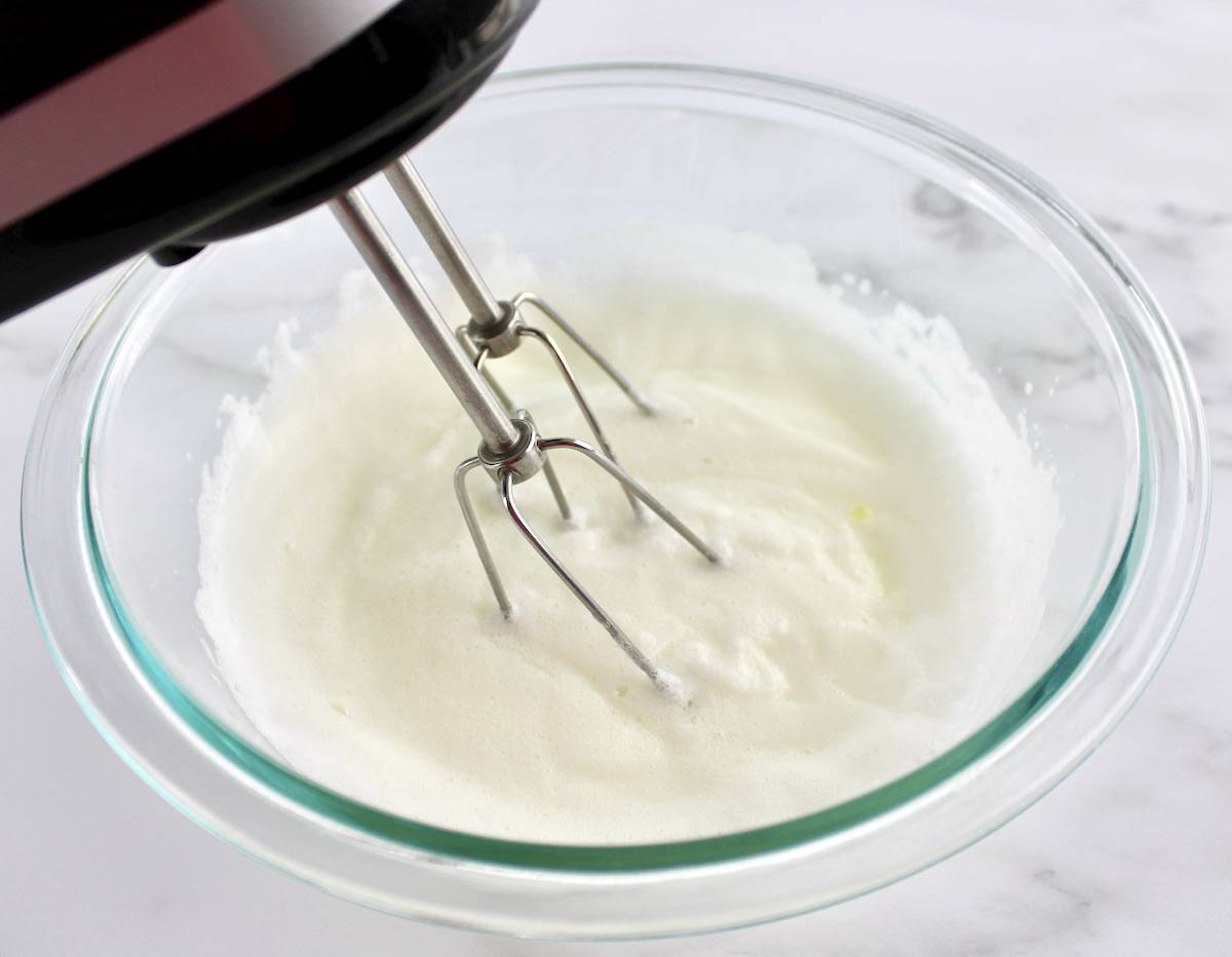 egg whites being whipped in glass bowl with hand mixer