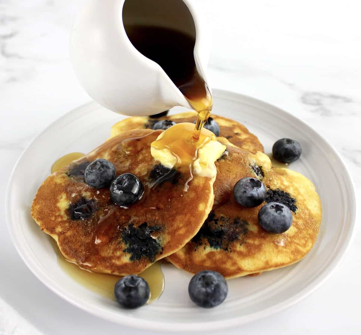 Keto Blueberry Pancakes on white plate with blueberries and syrup being poured on top