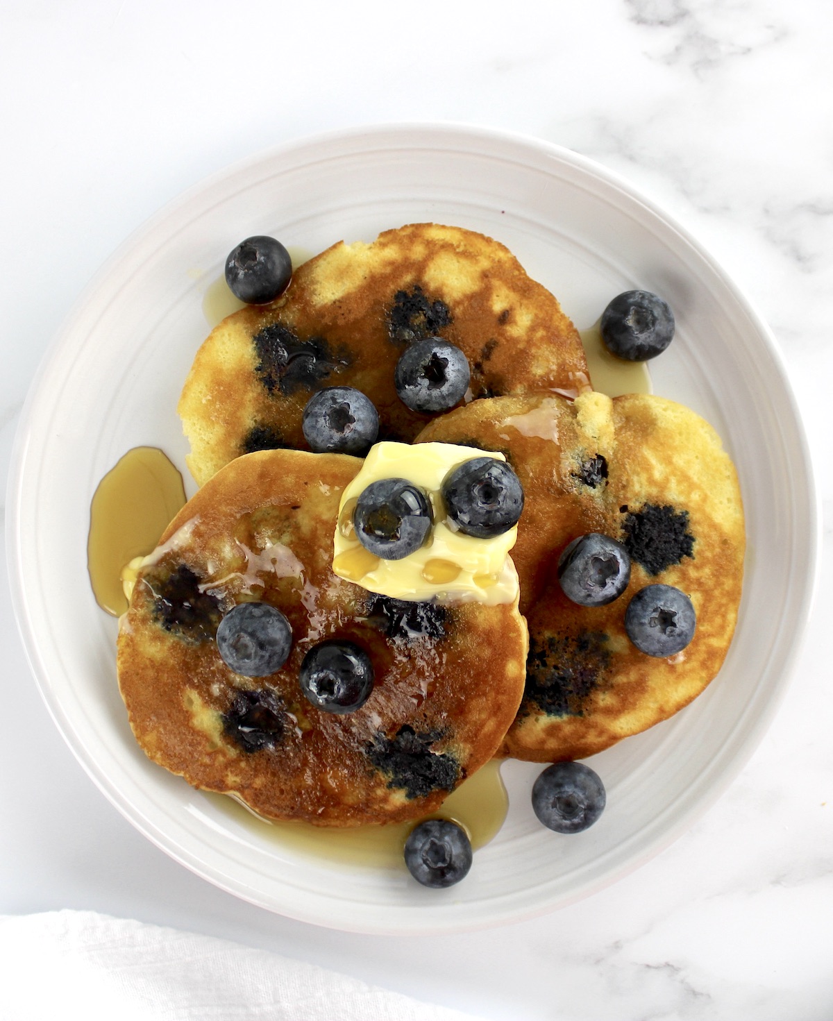 3 Keto Blueberry Pancakes on white plate with syrup and blueberries on top