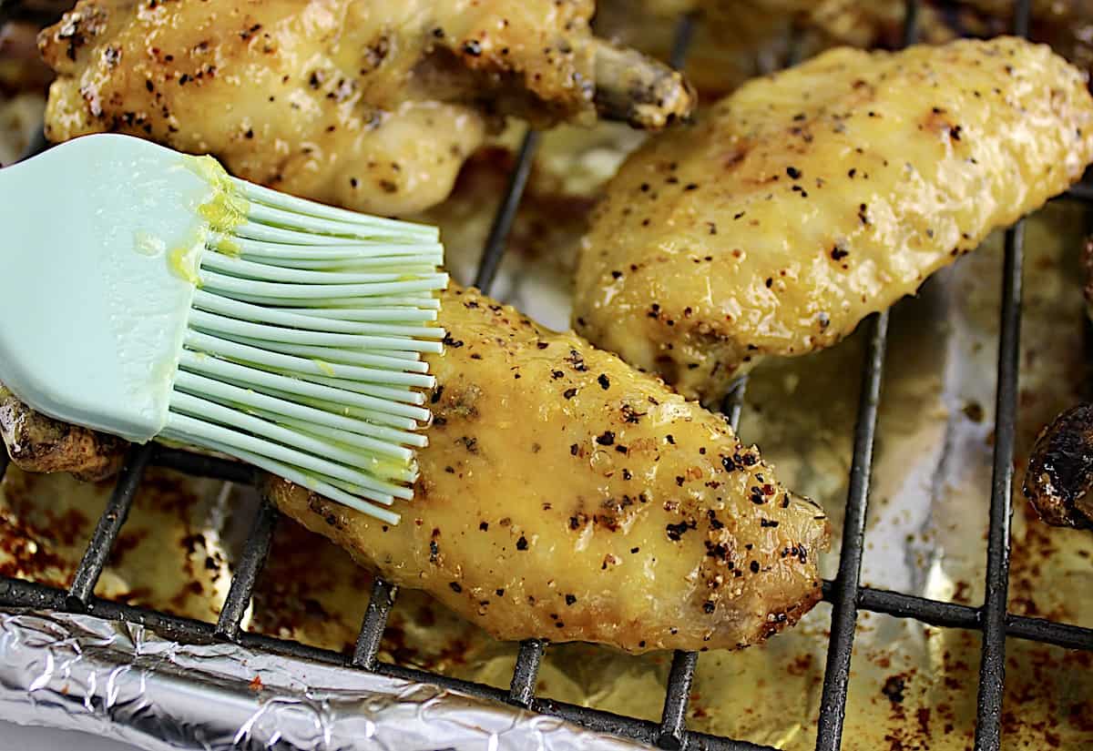 lemon pepper sauce being brushed over chicken wings on wire rack