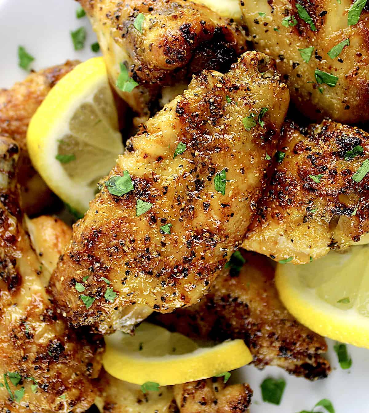 closeup of Lemon Pepper Chicken Wings on white plate with chopped parsley and lemon slices