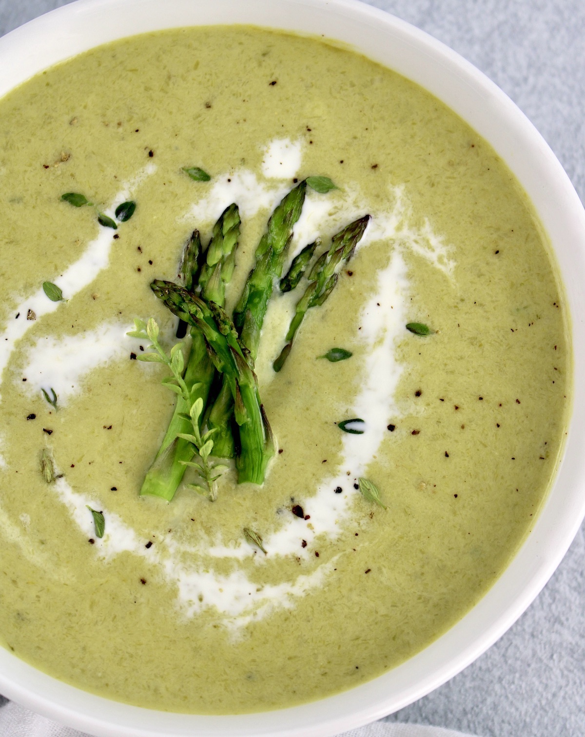 overhead view of Cream of Asparagus Soup with asparagus spears in center and swirl of cream around