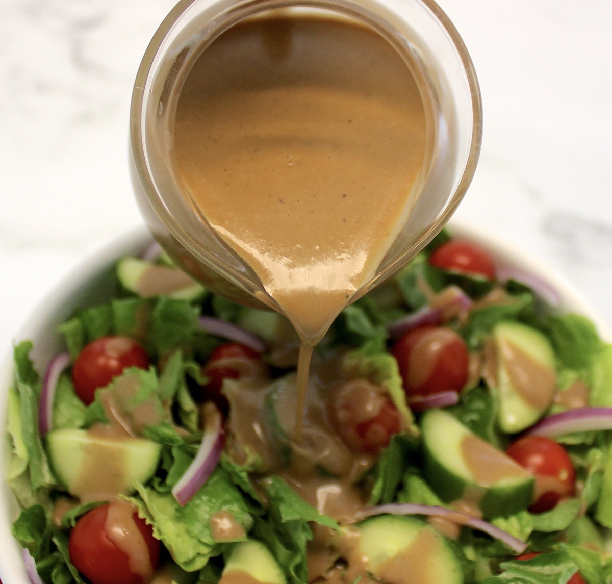 glass pitcher pouring Creamy Balsamic Dressing over salad