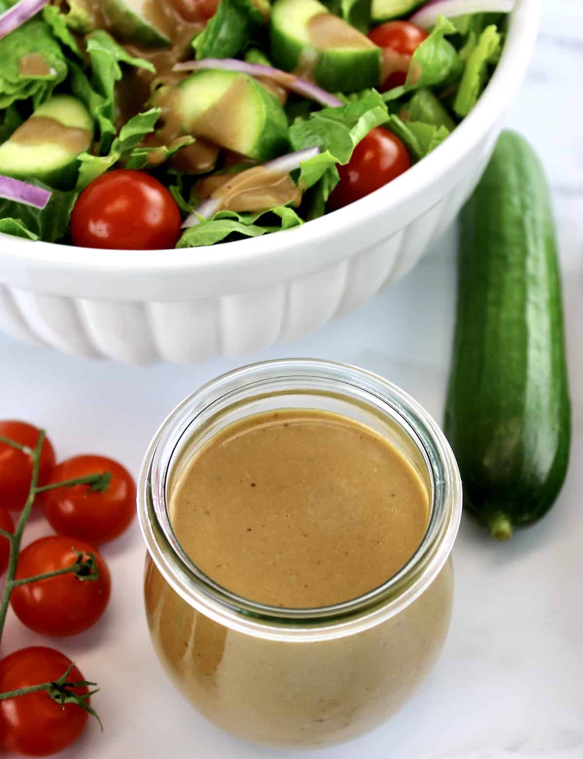 overhead view of Creamy Balsamic Dressing in open glass jar with salad in white bowl in background