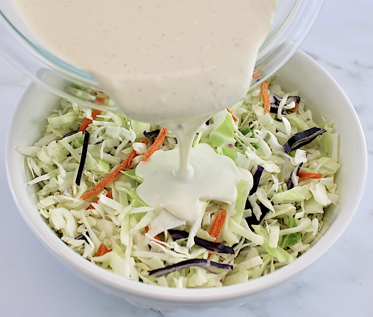 coleslaw dressing being poured over slaw mix in white bowl