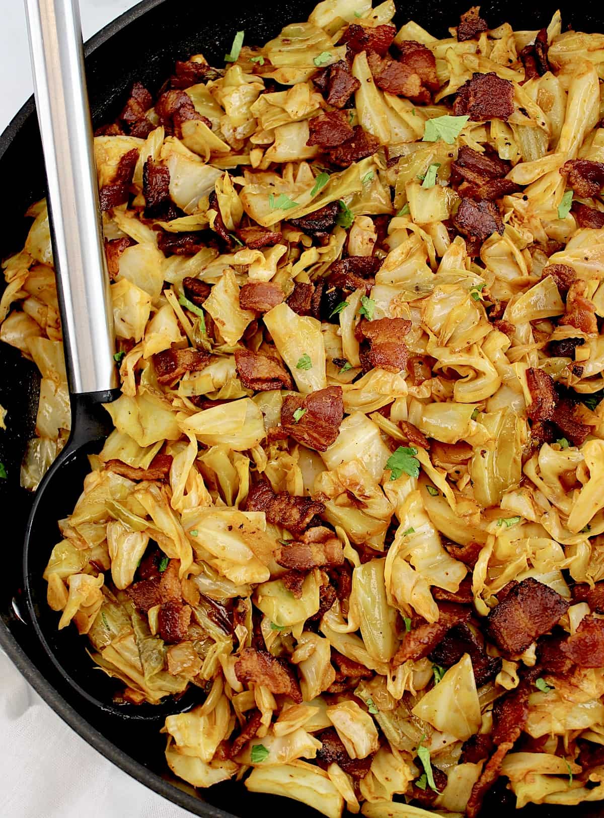 fried cabbage with bacon in skillet with serving spoon