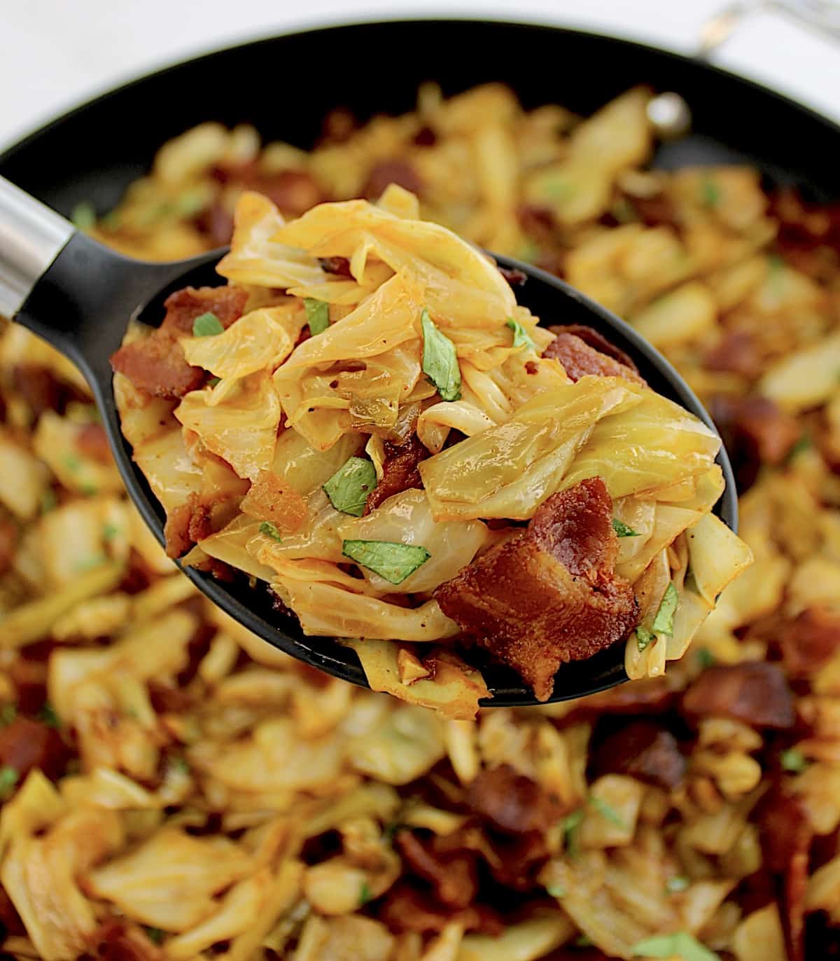 Fried Cabbage with Bacon in serving spoon over skillet