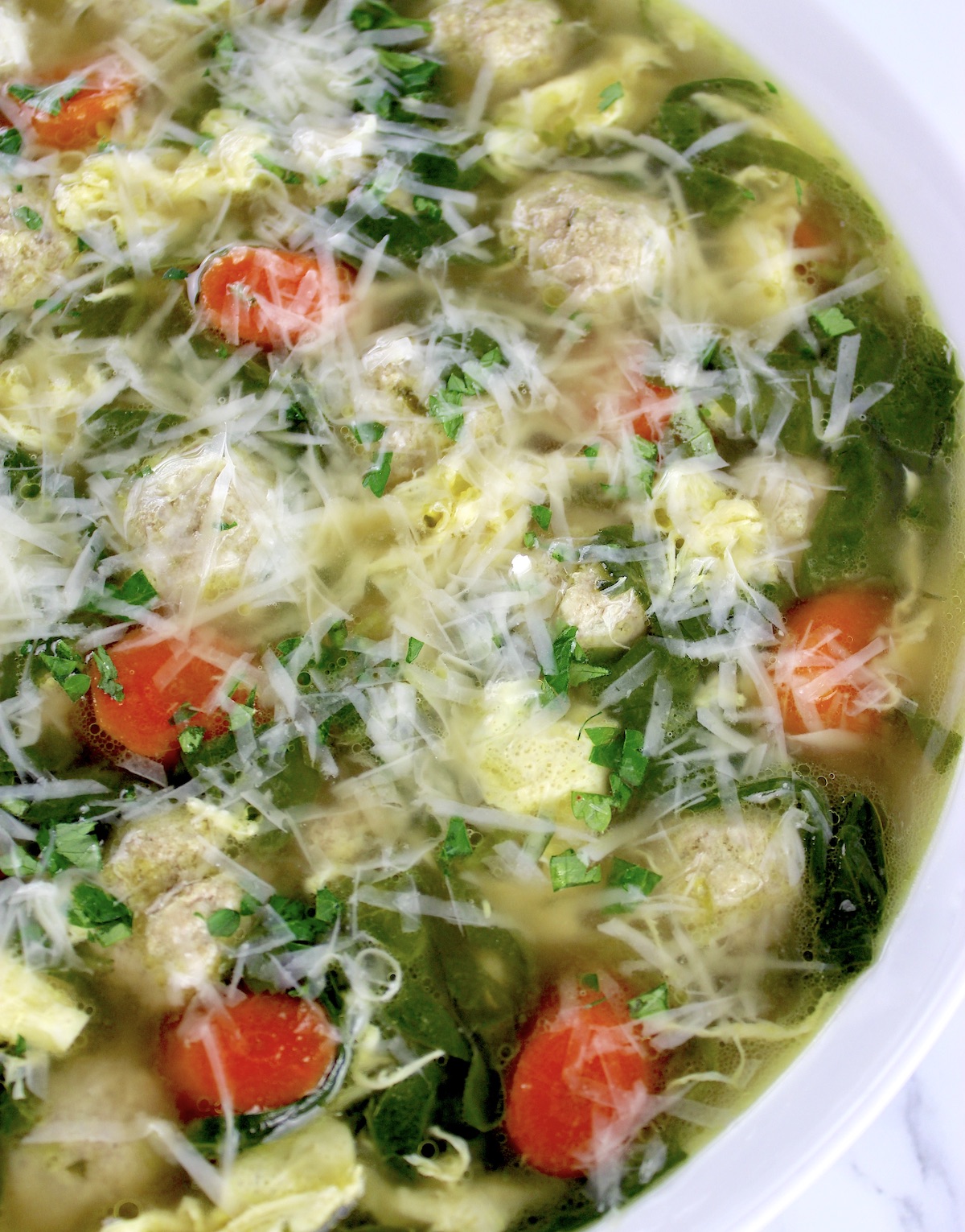 closeup of Italian Wedding Soup in white bowl with grated parmesan cheese