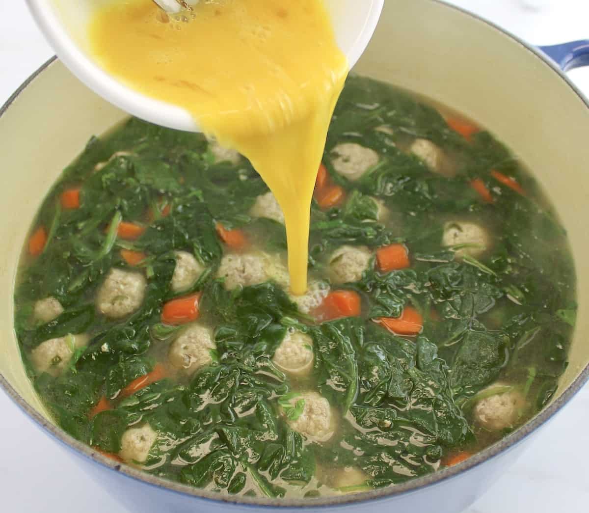 scrambled eggs being poured into Italian Wedding Soup in pot